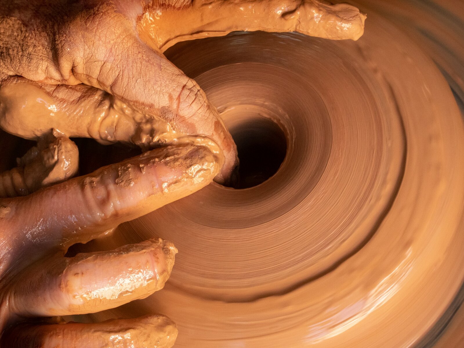 A potter shaping wet clay on the wheel, hands close up